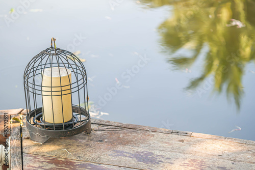 Home outdoor decoration with lamp inside birdcage on ancient wooden floor near the river