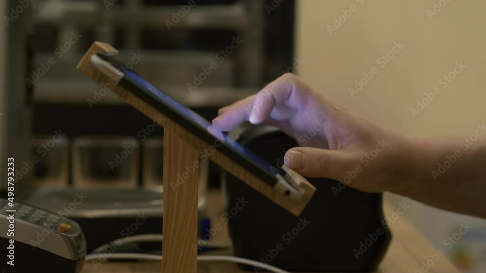 Hand of barista using touch screen cashier receives an order to customer at coffee shop, close up. Business service. Hand of barista using touch screen cashier receives an order to customer at coffee shop, close up. Business service.