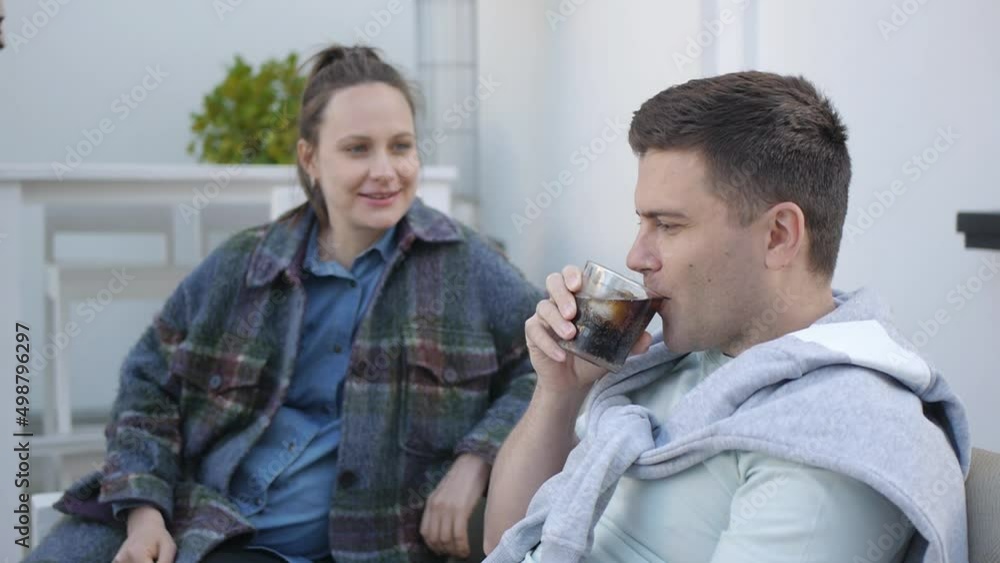 Young man drinking carbonated soft drink from the glass with ice and lemon slice. Pregnant woman and man at the cafe terrace. Young man drinking carbonated soft drink from the glass with ice and lemon slice. Pregnant woman and man at the cafe terrace.