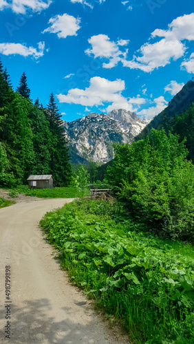 Alpine cottage and hiking path with scenic view on mountain peaks of Kamnik Savinja Alps in Carinthia, border Austria and Slovenia. Trail passing by a wooden shelter. Mountaineering. Freedom. Europe
