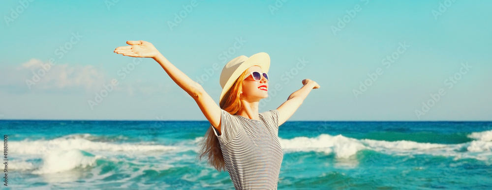 Happy smiling woman raising her hands up on the beach on sea background at summer day