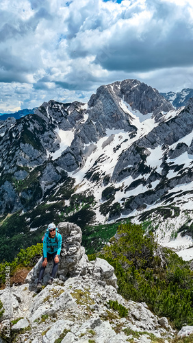 Woman with backpack and helmet resting on hiking path with scenic view on mountains Kamnik Savinja Alps in Carinthia, border Slovenia Austria. Velika Baba, Vellacher Kotschna. Mountaineering. Freedom