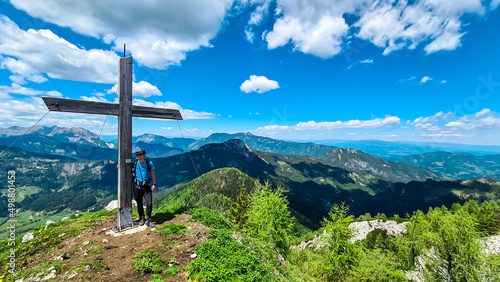 Happy man arriving at the summit cross of Goli Vrh and enjoying the scenic view on the mountains of Kamnik Savinja Alps in Carinthia, border Slovenia Austria. Vellacher Kotschna. High altitude freedom photo
