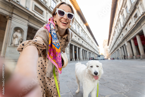 Young happy woman takes selfie with a dog on Uffizi square visiting museum in famous italian city Florence. Female tourist traveling italian landmarks