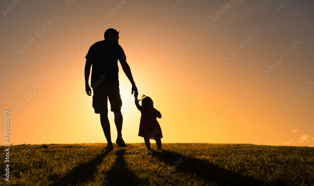 Silhouette of father holding his child's hand walking into the sunset. Fatherhood, parenting concept.  - obrazy, fototapety, plakaty 