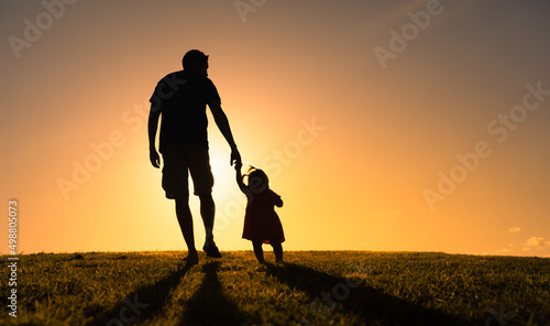 Silhouette of father holding his child's hand walking into the sunset. Fatherhood, parenting concept.  photo