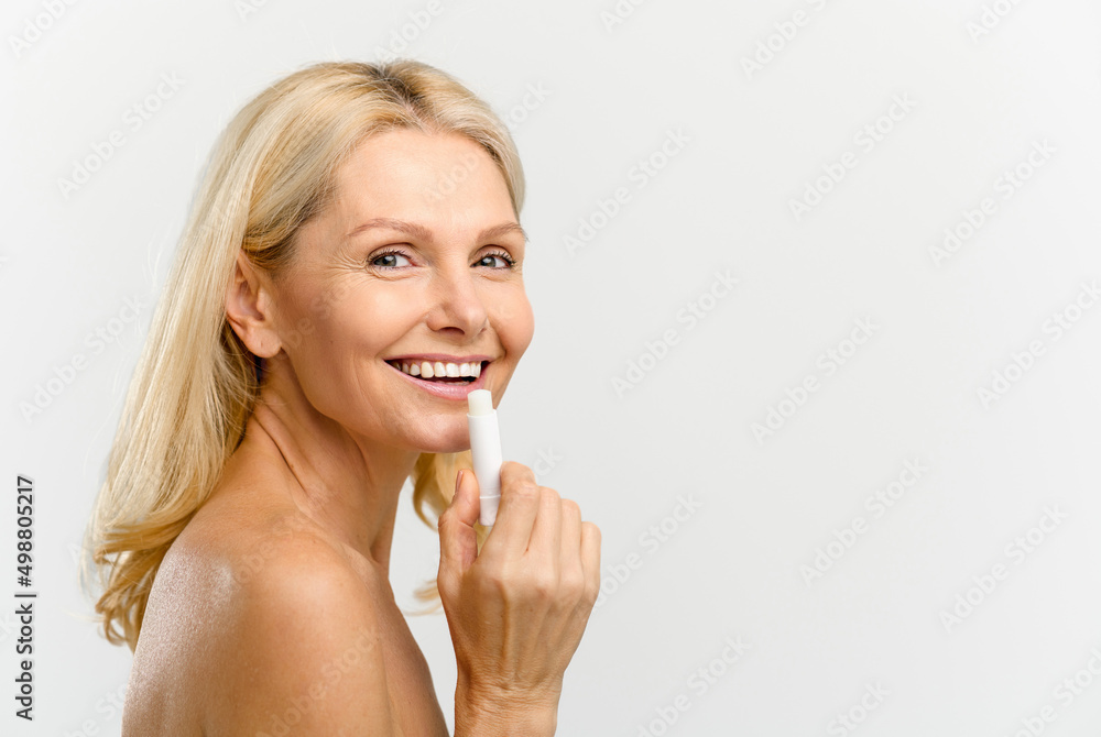 Happy and optimistic beautiful middle age woman applying natural lip balm isolated on white. Charming blonde lady using moisturizing lipstick, treatment balm. Advertising concept Happy and optimistic beautiful middle age woman applying natural lip balm isolated on white. Charming blonde lady using moisturizing lipstick, treatment balm. Advertising concept