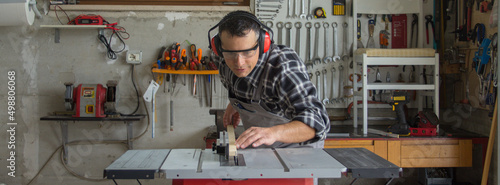 
Carpenter at work in his workshop while cutting pieces of wood with a bench saw. Furniture restoration work. Horizontal banner 