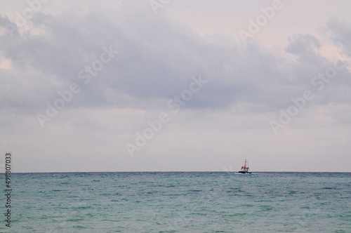 Far out to sea, a boat floats on the waves against the background of a high cloudy sky.