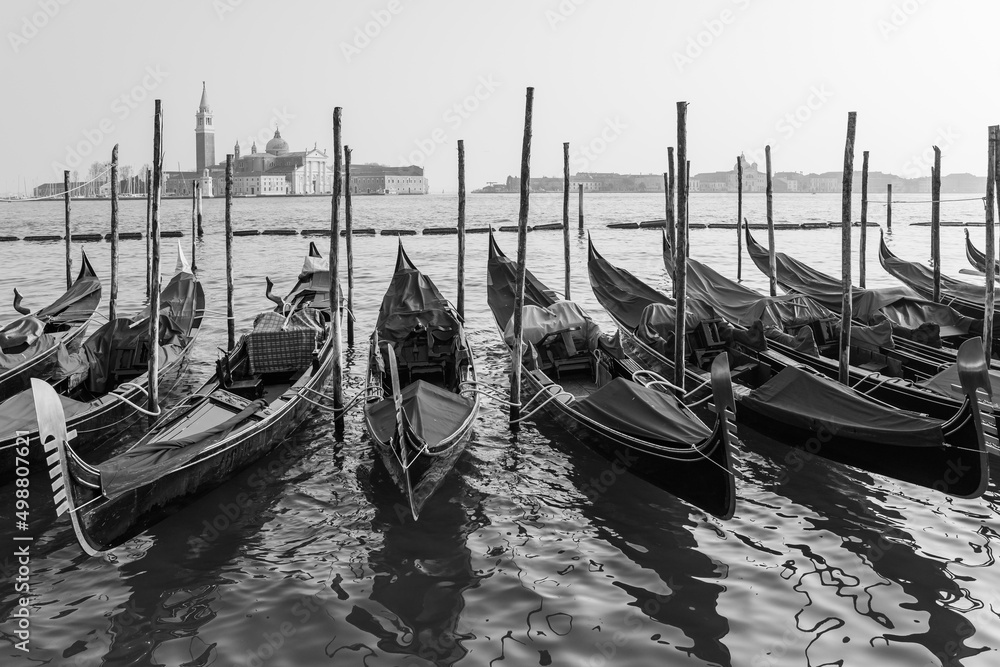 black and white photo of gondolas parked by the grand canal in Venice, Italy with the church of Saint Giorgio Maggiore in the background
