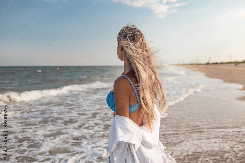 Portrait of a girl in a blue swimsuit and white shirt against the background of the blue sea and clear sky Portrait of a girl in a blue swimsuit and white shirt against the background of the blue sea and clear sky