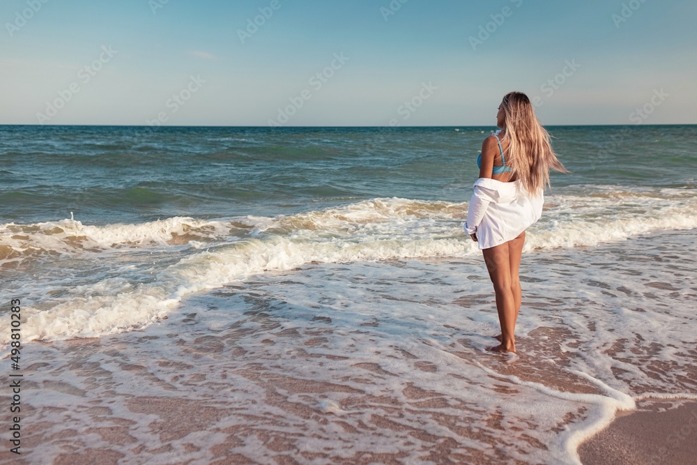 A tanned girl in a blue swimsuit and a light shirt enjoys the summer at the seaside A tanned girl in a blue swimsuit and a light shirt enjoys the summer at the seaside