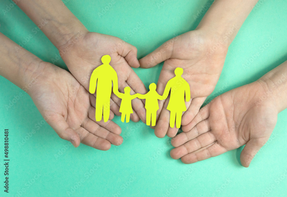 Children's hands hold a family cut out of paper on a green background. Children in the family concept.Big friendly family. Children dream of a big family. Children's hands hold a family cut out of paper on a green background. Children in the family concept.Big friendly family. Children dream of a big family.
