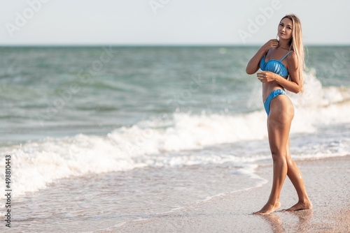 A girl with blond hair in a bluish swimsuit walks along the beach