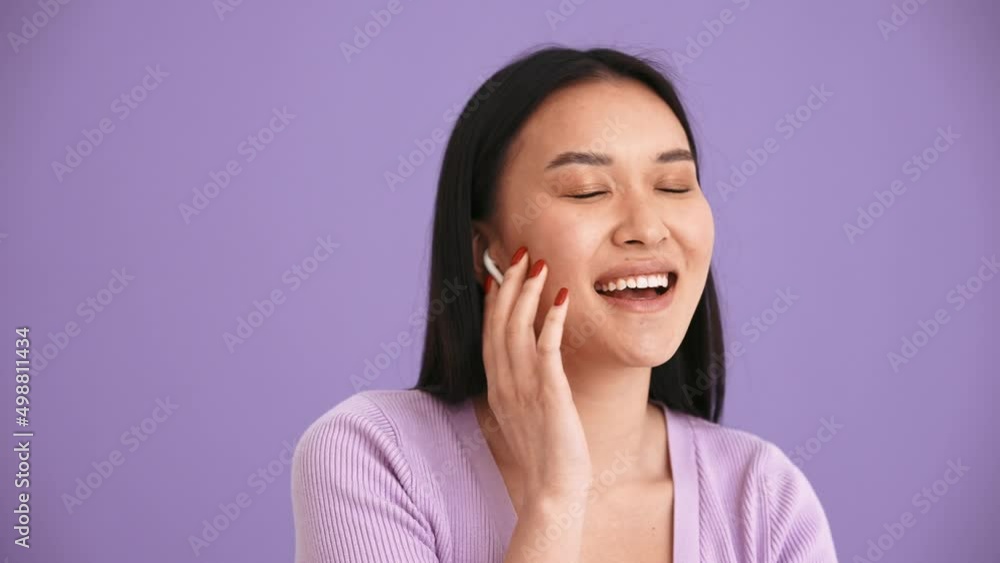 Smiling Asian brunette woman wearing purple t-shirt listening music in headphones in the purple studio Smiling Asian brunette woman wearing purple t-shirt listening music in headphones in the purple studio