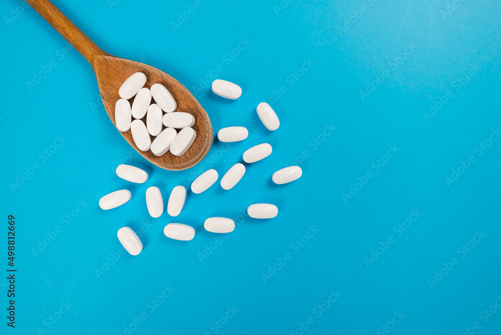 Top view of white pills in a wooden spoon. Top view of white pills in a wooden spoon.