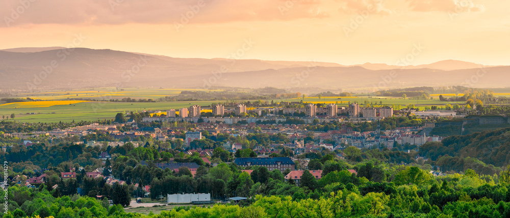 Kłodzko, panorama of the city in the valley against the background  of the mountains lit by bright sun at sunset.