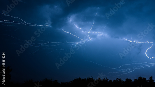 Electrical discharges during a summer storm, branched lightning bolts in the night sky.