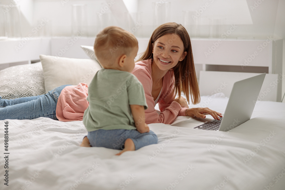 Happy lady using laptop while looking at her baby son