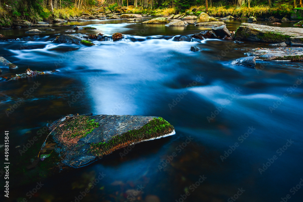 The calm water flows along the rocky bed of the mountain river, the rocks covered with moss are visible on a sunny day.