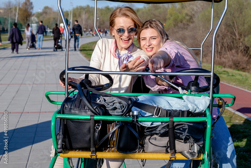 Mother and daughter having fun riding a roofed tandem bicycle or a quadricycle with a steering wheel on a promenade. photo