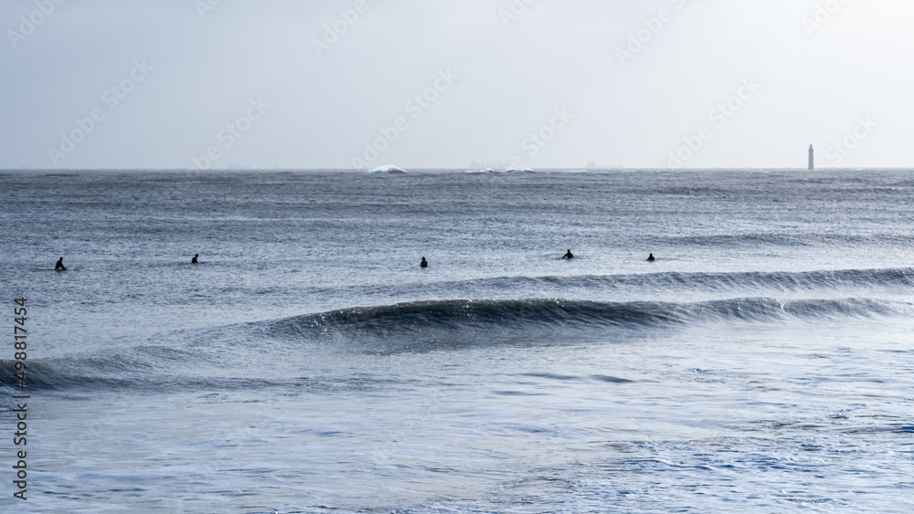 silhouette of surfers in waves with Chauveau lighthouse, the famous lighthouse near La Rochelle and Re island silhouette of surfers in waves with Chauveau lighthouse, the famous lighthouse near La Rochelle and Re island