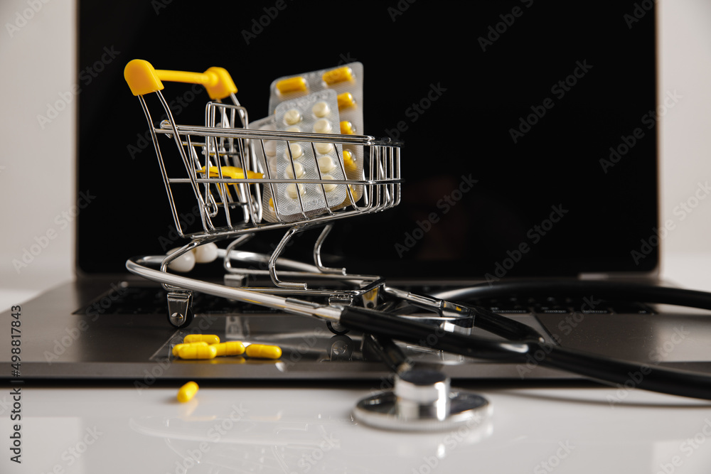 Online pharmacy. Trolley with medicines and stethoscope on a laptop
