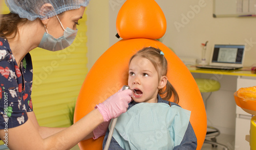 A beautiful little girl with a toy is visiting the dentist's office. She is sitting on a chair and the dentist is soothing the child