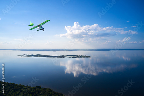 A full-flowing flat river with forested banks. There is a small island in the middle of the river. The white cloud is beautifully reflected in the water. Shooting from a drone.