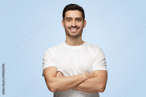 Young smiling attractive man stands with arms crossed isolated on blue background