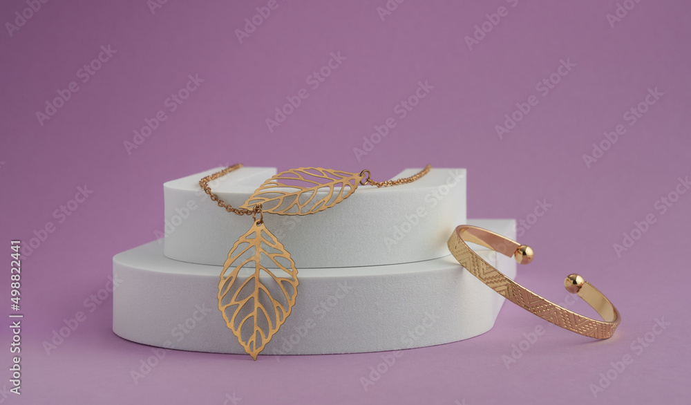 Leaf shape Necklace pendant and geometric pattern bracelet on white podium on purple background Leaf shape Necklace pendant and geometric pattern bracelet on white podium on purple background