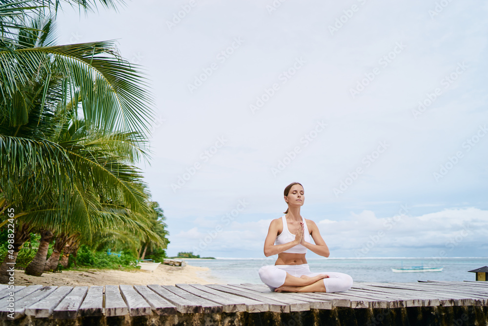 Yoga and meditation. Relaxed young woman in lotus pose on wooden deck with sea view.