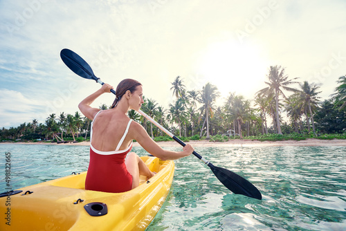 Young woman paddling the sea kayak in the tropical calm lagoon.