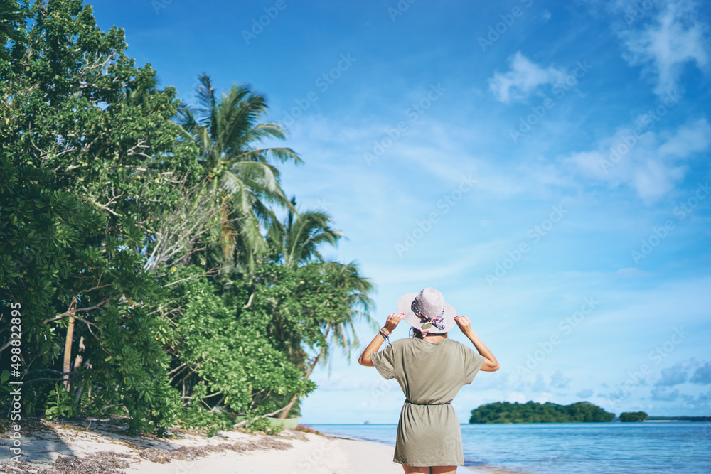 Vacation on the seashore. Back view of young woman walking away on the beautiful tropical white sand.