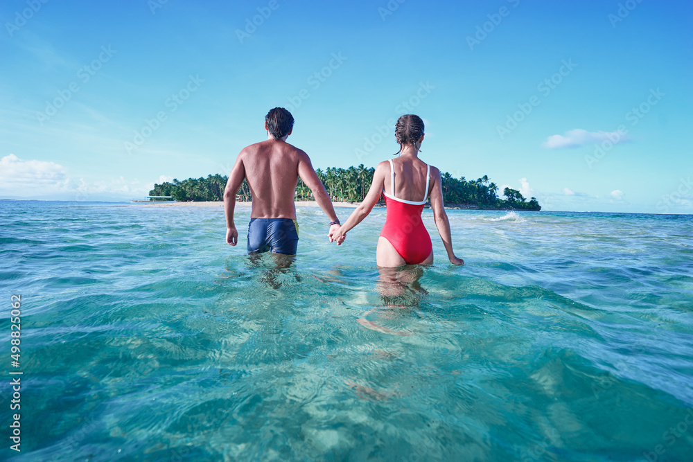 Honey moon on the sea shore. Back view of loving couple bathing together on beautiful tropical island beach.