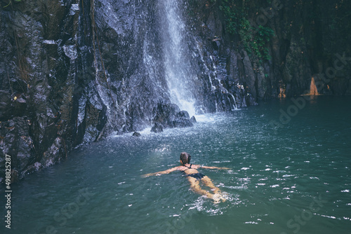 Travel and nature. Young woman swimming in tropical waterfall pool.