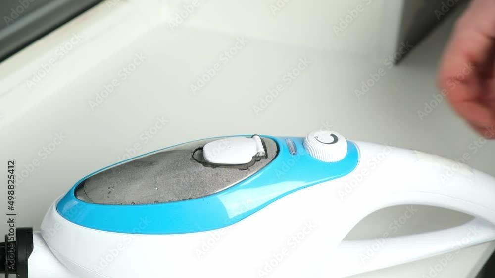 A man pours distilled water into a steam cleaner container using a