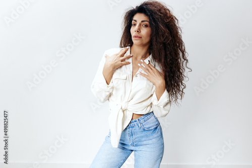 Serious Sexy Stylish Curly Pensive Latin Female Lady With Long Afro Hair in White Shirt Touching Collar Looking At Camera Isolated At White Studio Background. Banner Mockup copy space free place
