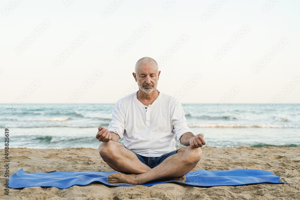 Senior man doing yoga meditation outdoor with beach on background - Focus on face