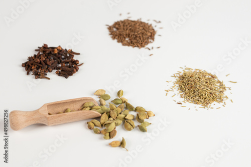 cardamom in a wooden spoon with other spices on a white background