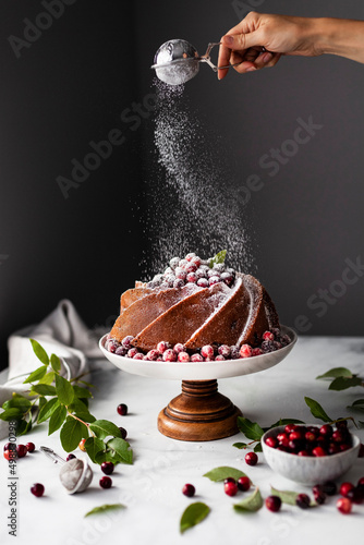 A baker dusting a cranberry orange bundt cake with powdered sugar