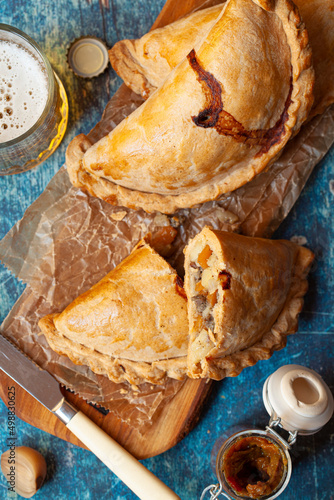 Several Cornish pasties on a wooden board served with pickled onions.