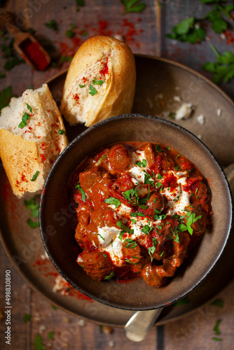 A bowl of beef goulash topped with soured cream and parsley with a side of cursty bread. photo