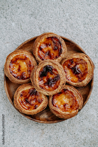 Six Pasteis de nata (small traditional Portuguese cake) placed on a wooden plate, on grey ciment background. Top view photo