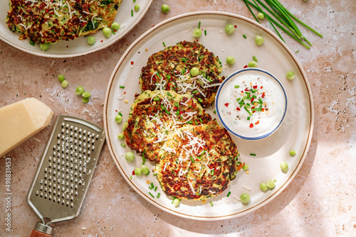 zucchini pancake, peas, chives, grated parmesan,cheese grinder, pot of spicy cream, in white plate photo