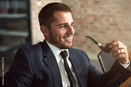 Suave and successful. Shot of a stylish businessman smoking a pipe in the office.