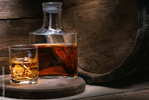 Bourbon whiskey is strong alcoholic beverage prepared by Irish monk. Grain whiskey from Scotland in wooden old barrel is poured whiskey into decanter and glass of ice of amber color.