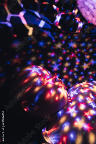 Vertical shot of a baby boy looking at his star projector lamp covered with colorful light stars. High quality photo photo