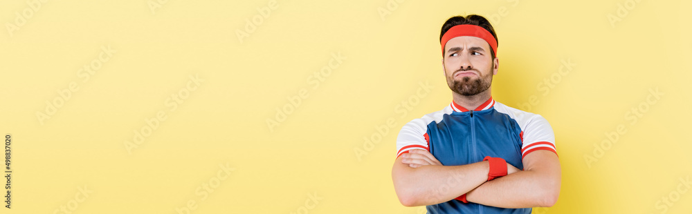 Fototapeta premium Pensive sportsman crossing arms and looking away isolated on yellow, banner.