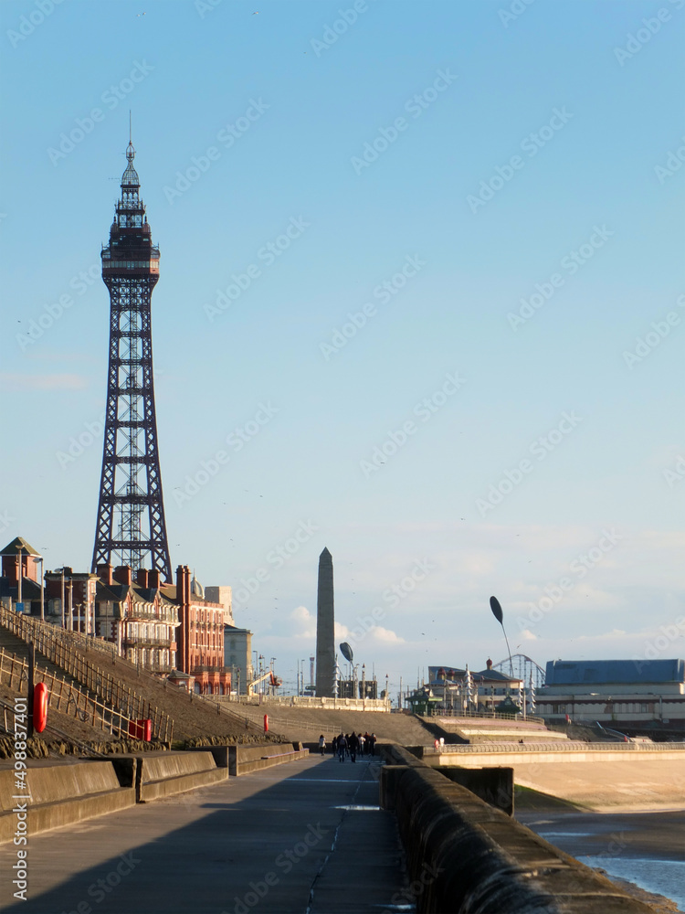 view of blackpool tower from the promenade with town buildings in afternoon sunlight
